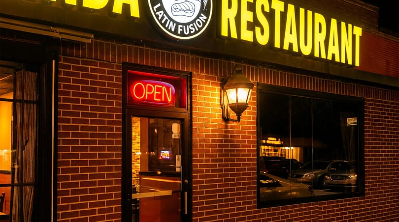 Brightly lit brick Latin Fusion restaurant exterior at night with an 'OPEN' sign and glowing lantern.