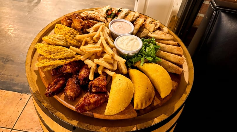 Assorted fried appetizers including wings, fries, empanadas, and quesadillas with sauces on a wooden platter.