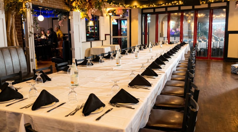 Elegantly set long dining table with black napkins and water bottles in a warm restaurant interior.